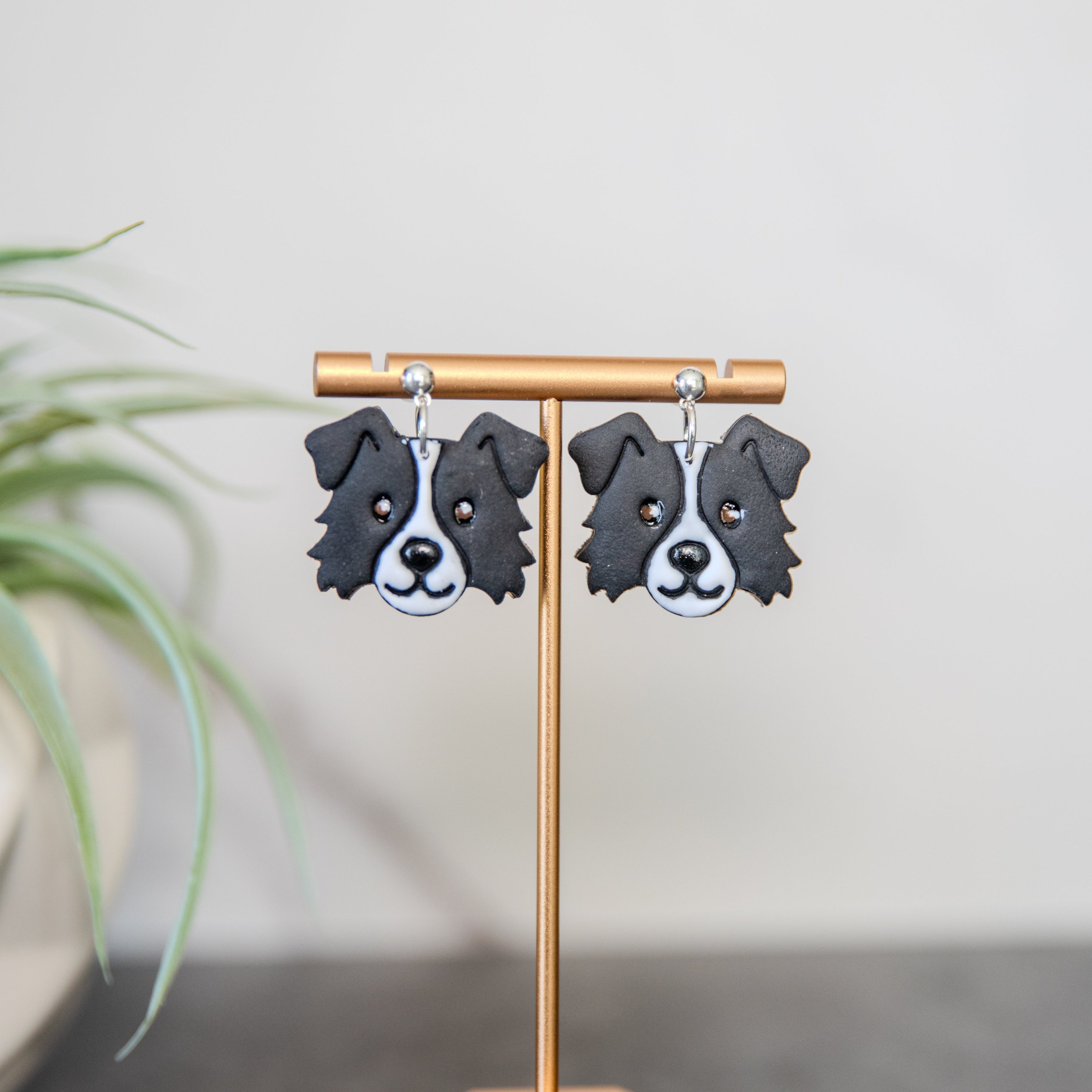 Border collie Dog-shaped earrings on a stand with a plant in the background