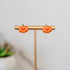 Pumpkin-shaped earrings on a gold stand with a blurred plant in the background