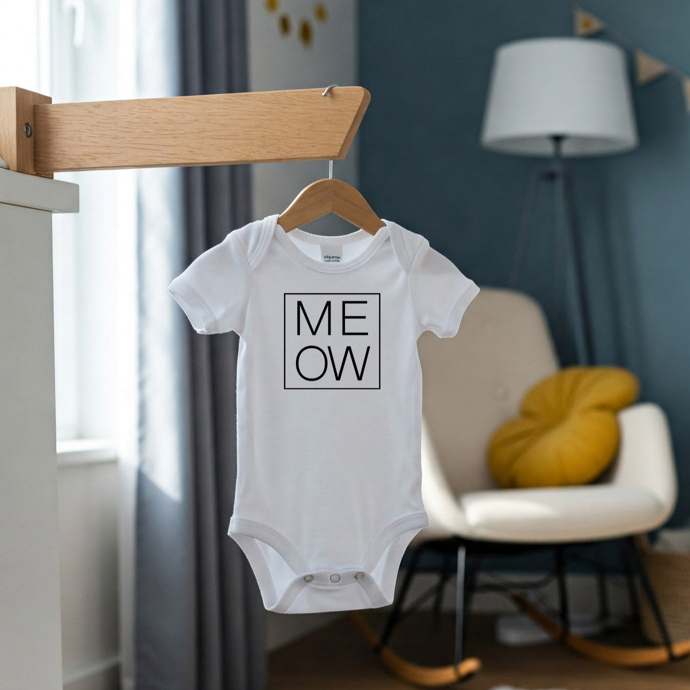 Baby onesie with 'MEOW' print hanging in a nursery room