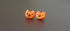Pair of orange cat-shaped earrings on a reflective gray surface