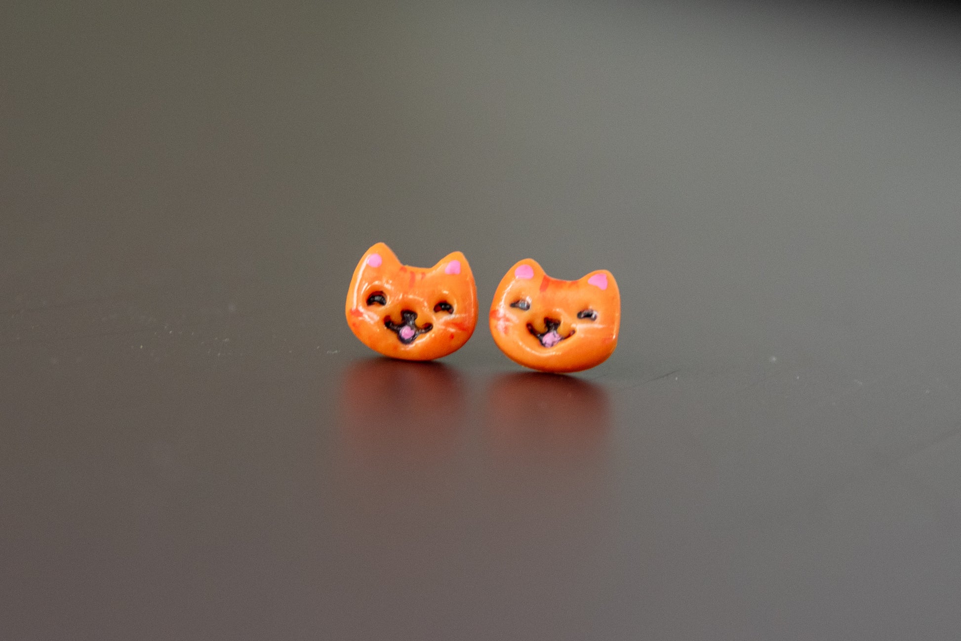 Pair of orange cat-shaped earrings on a reflective gray surface