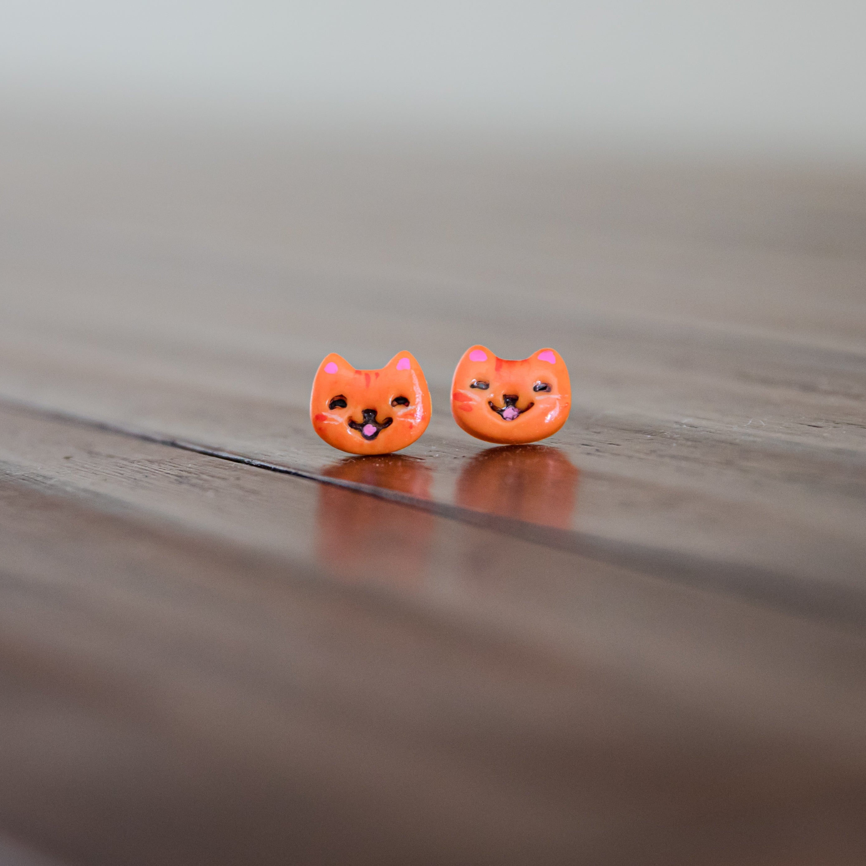 Two small orange cat-shaped earrings on a wooden surface.