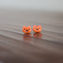 Two small orange cat-shaped earrings on a wooden surface.