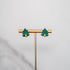 Pair of Christmas tree earrings on a gold stand against a gray background