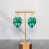 Green leaf-shaped earrings on a gold stand against a gray background