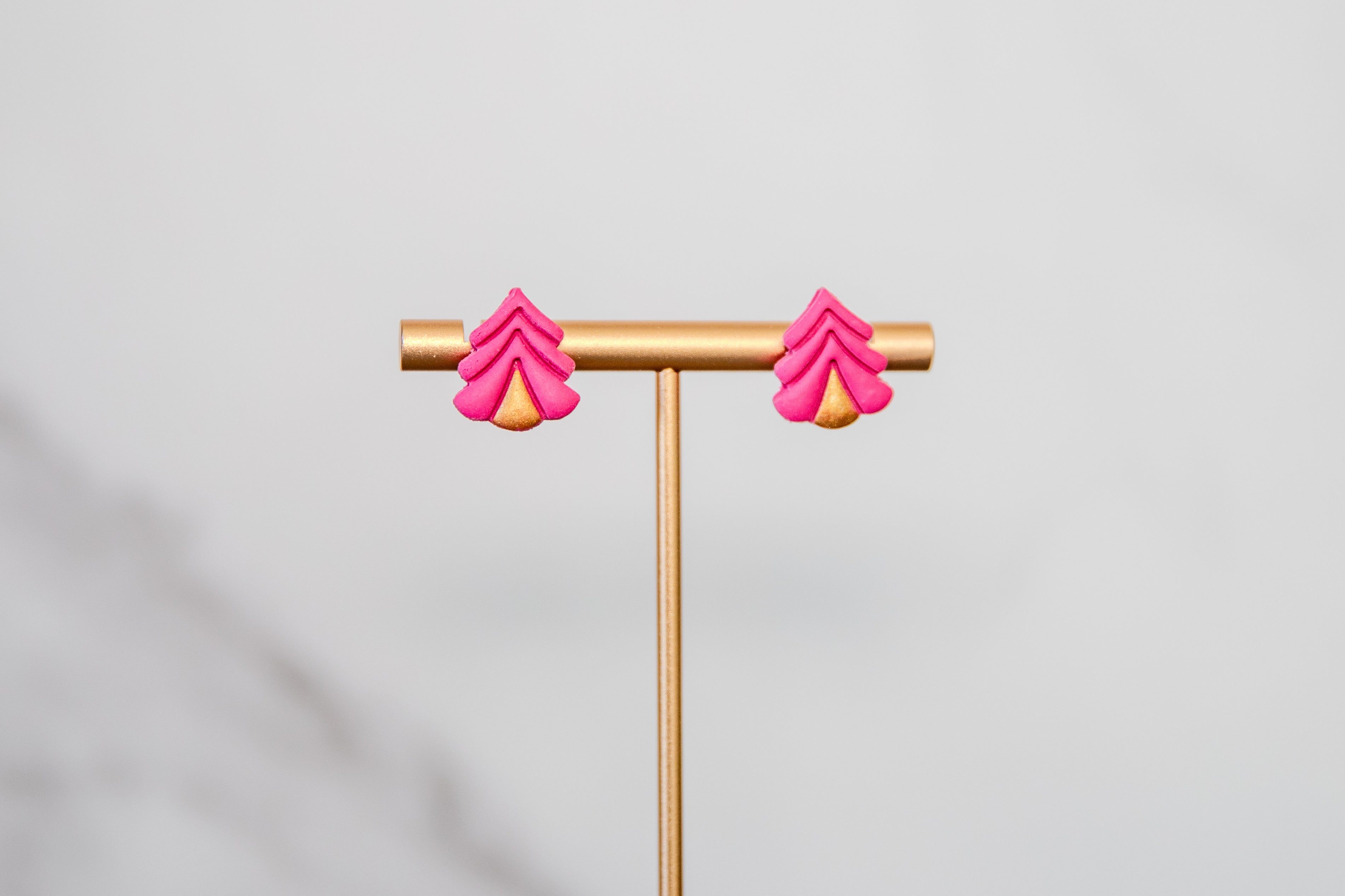 Pink tree-shaped earrings on a gold earring stand against a light gray background