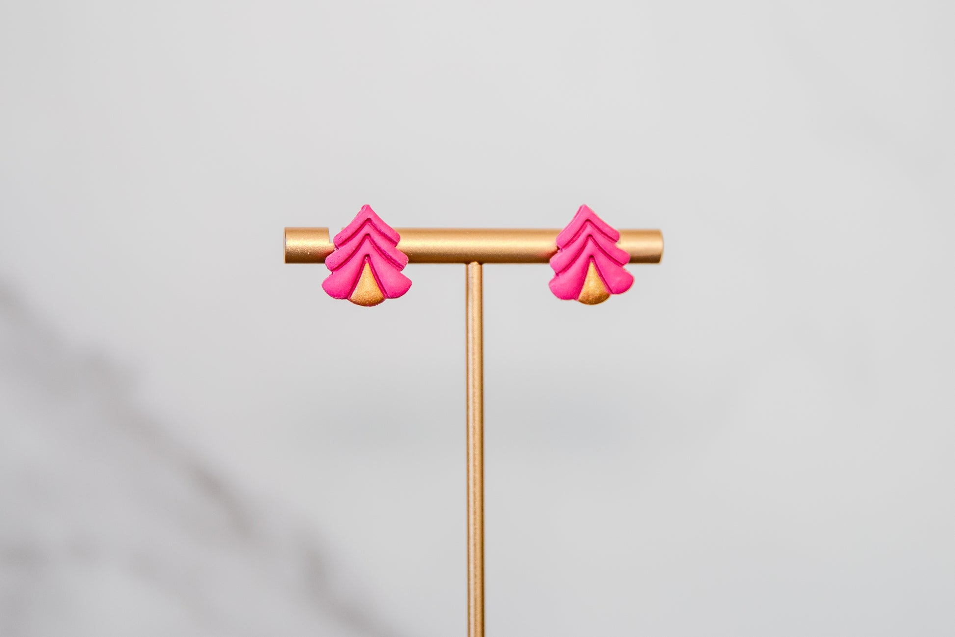 Pink tree-shaped earrings on a gold earring stand against a light gray background