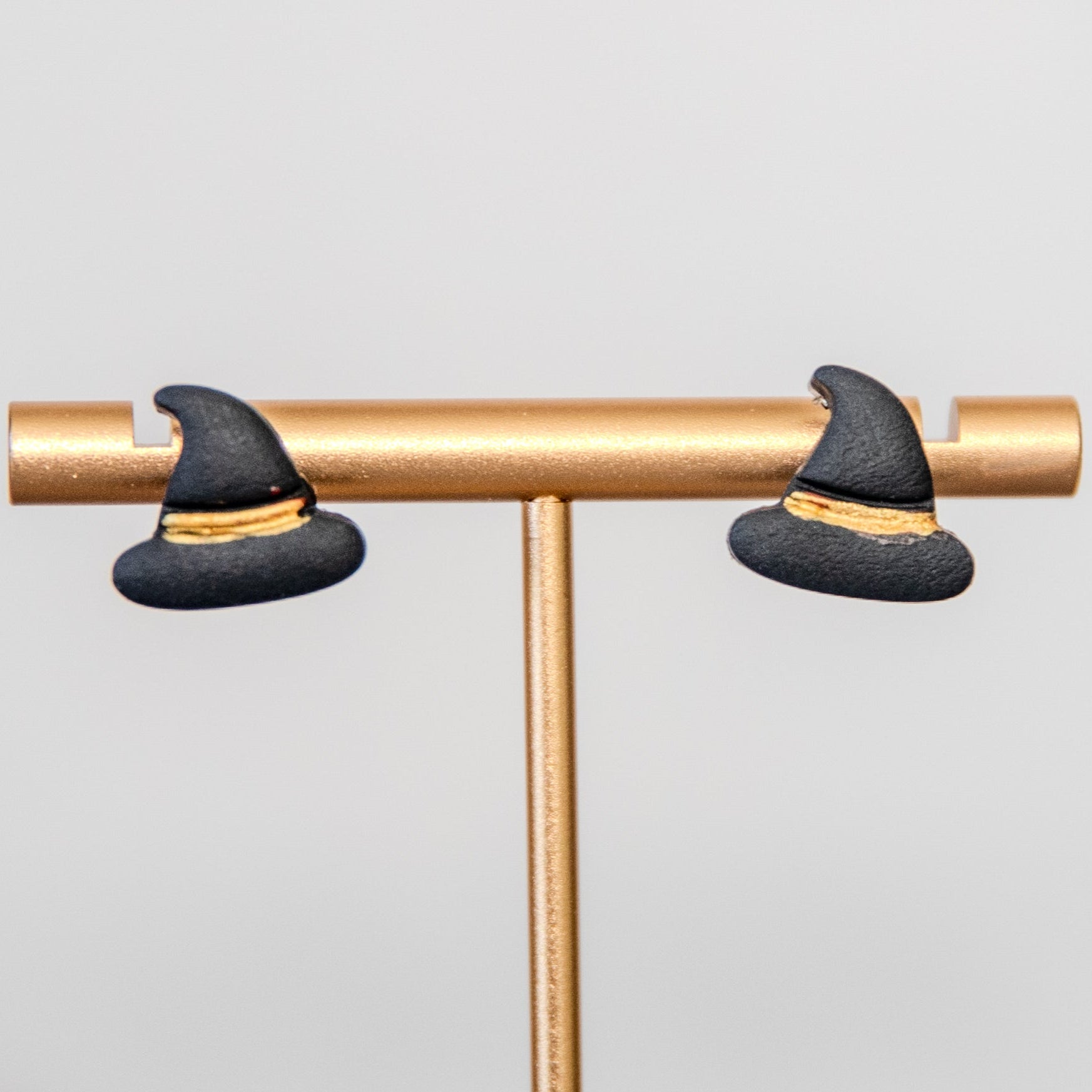 Witch hat earrings on a gold stand against a light gray background