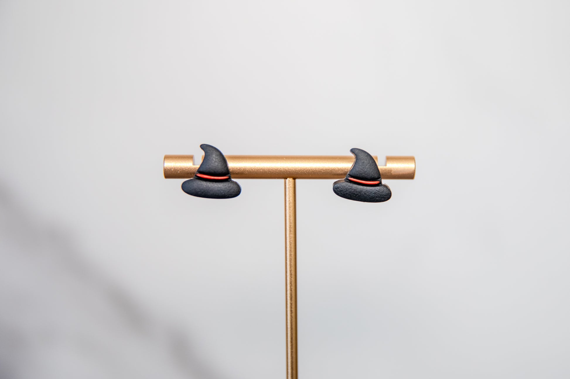 Two black witch hats on a gold stand against a light gray background