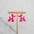 Pink balloon dog-shaped earrings on a gold stand against a gray background