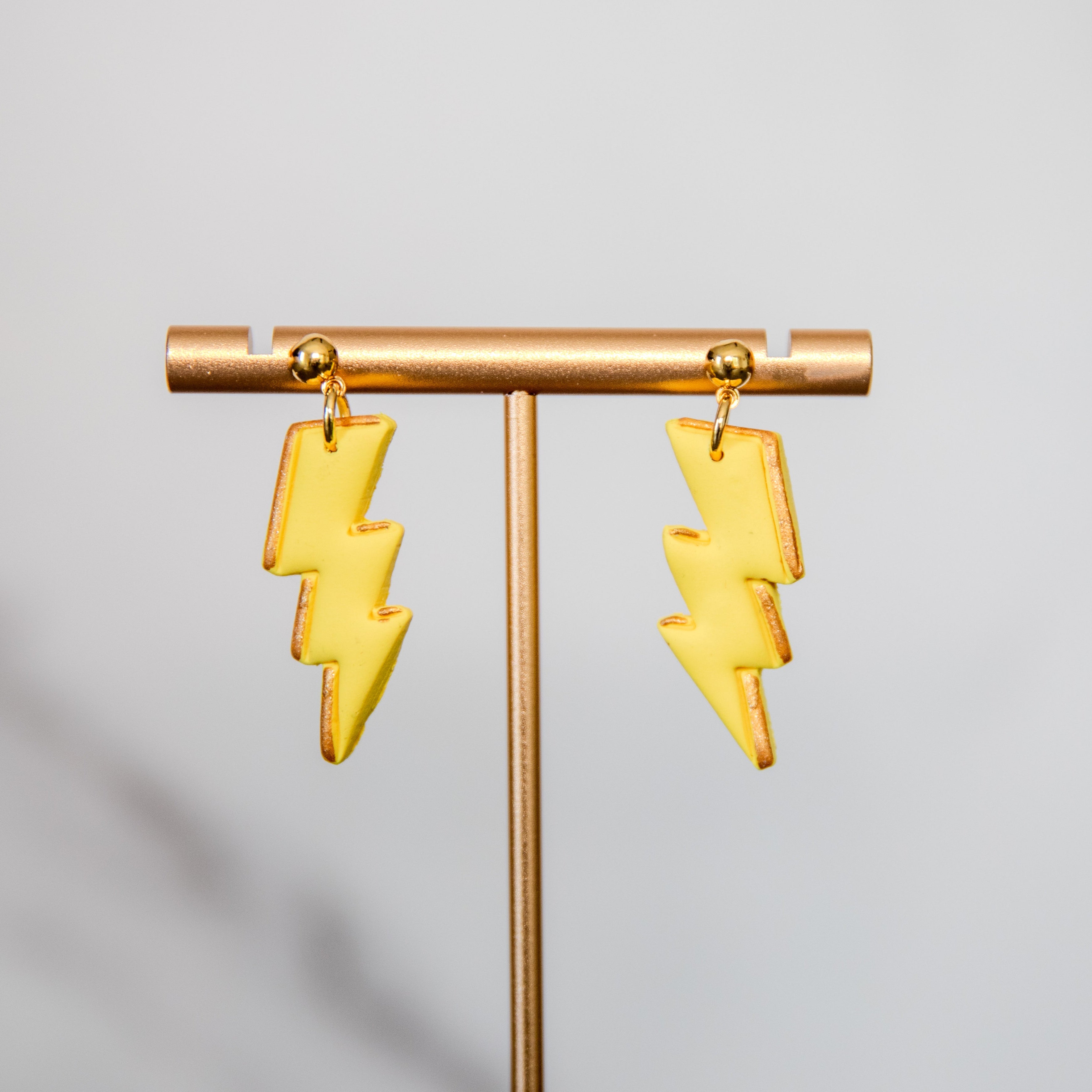Yellow lightning bolt earrings on a gold stand against a gray background