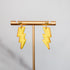 Yellow lightning bolt earrings on a gold stand against a gray background