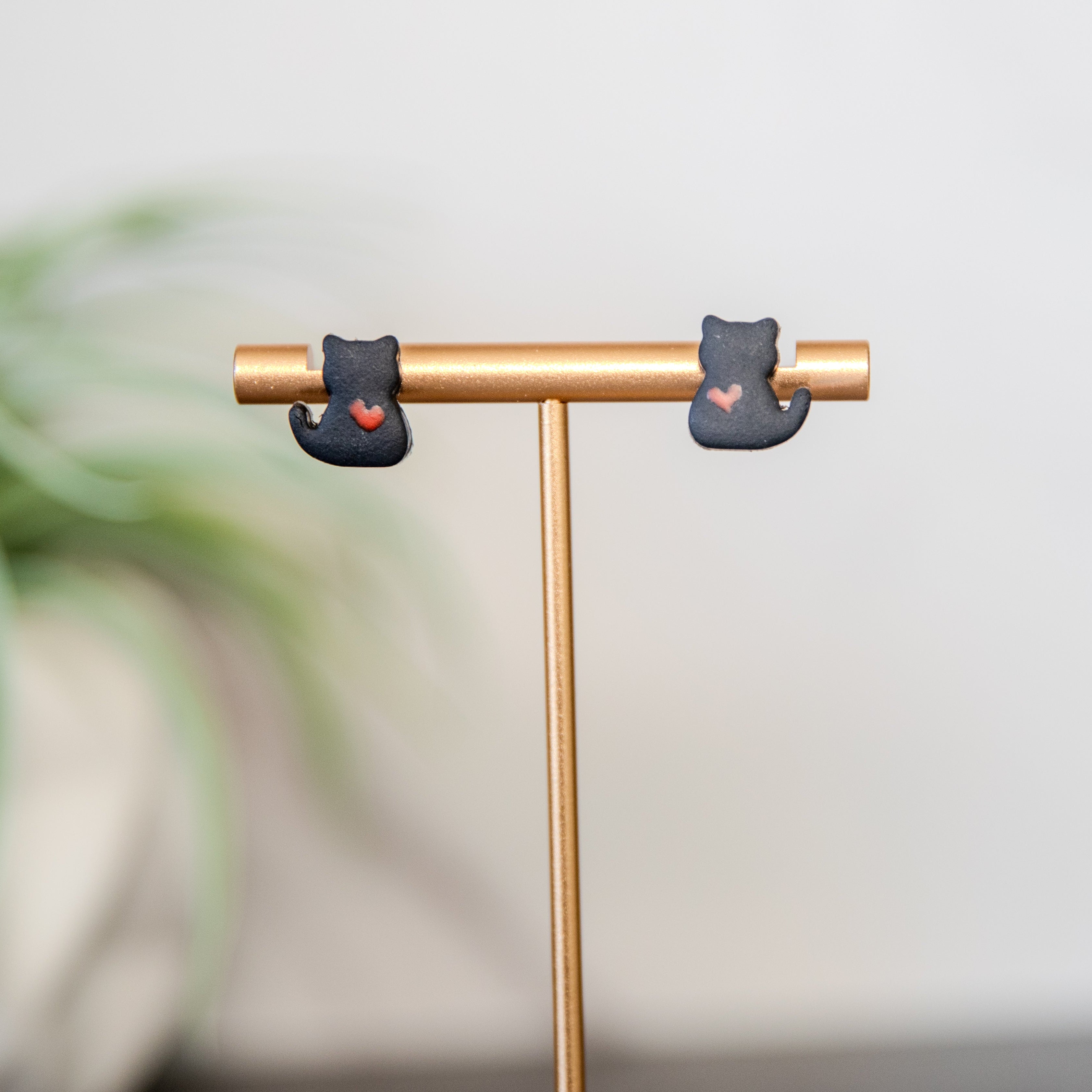 black Cat-shaped earrings on a gold stand with a blurred plant in the background