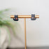black Cat-shaped earrings on a gold stand with a blurred plant in the background
