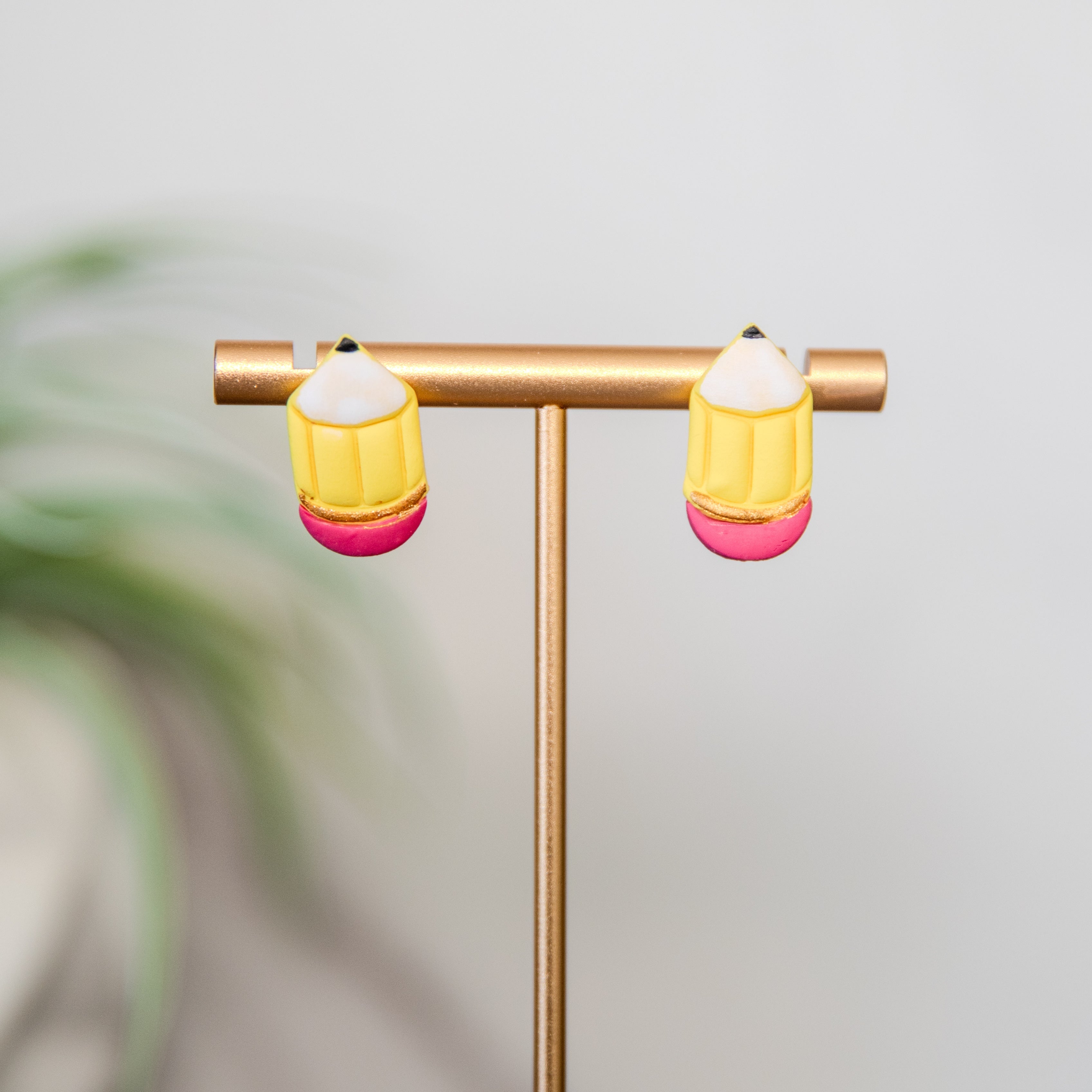 Pair of pencil earrings on a gold stand with a blurred plant in the background