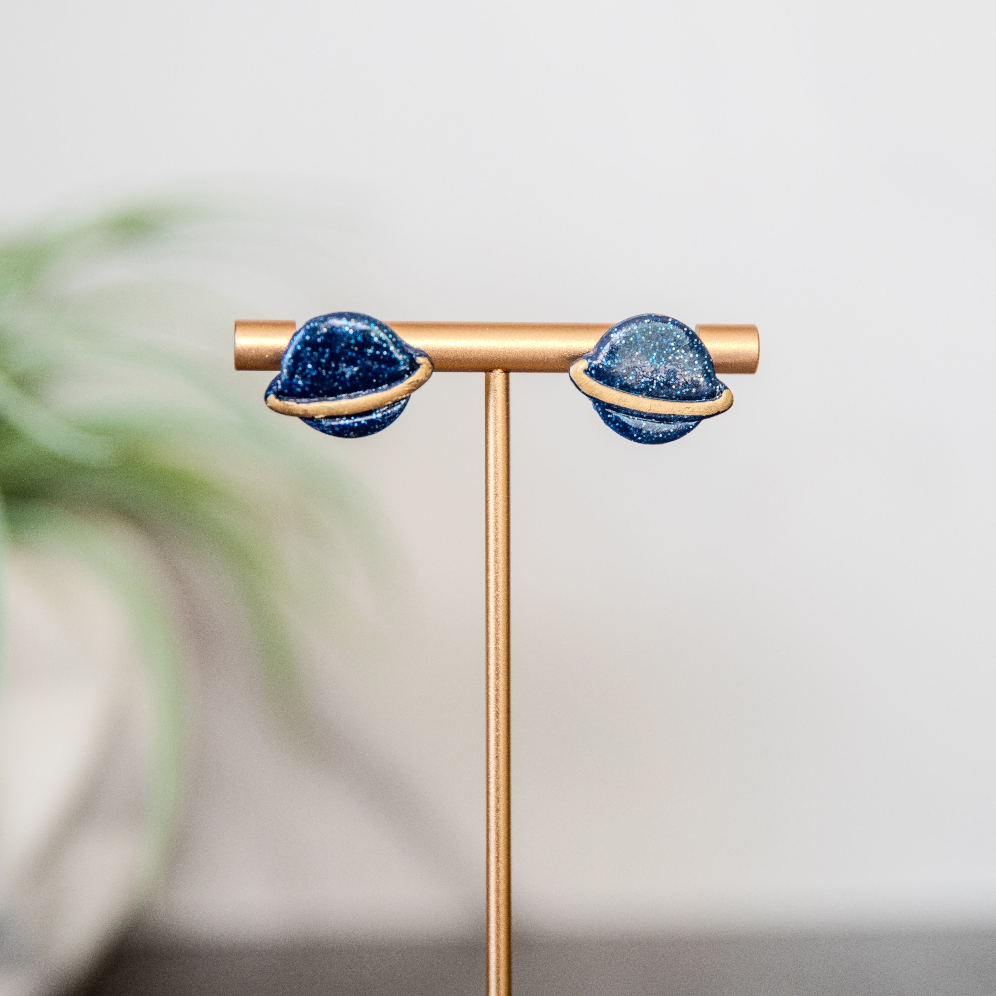 Pair of blue earrings on a gold stand with a blurred plant in the background