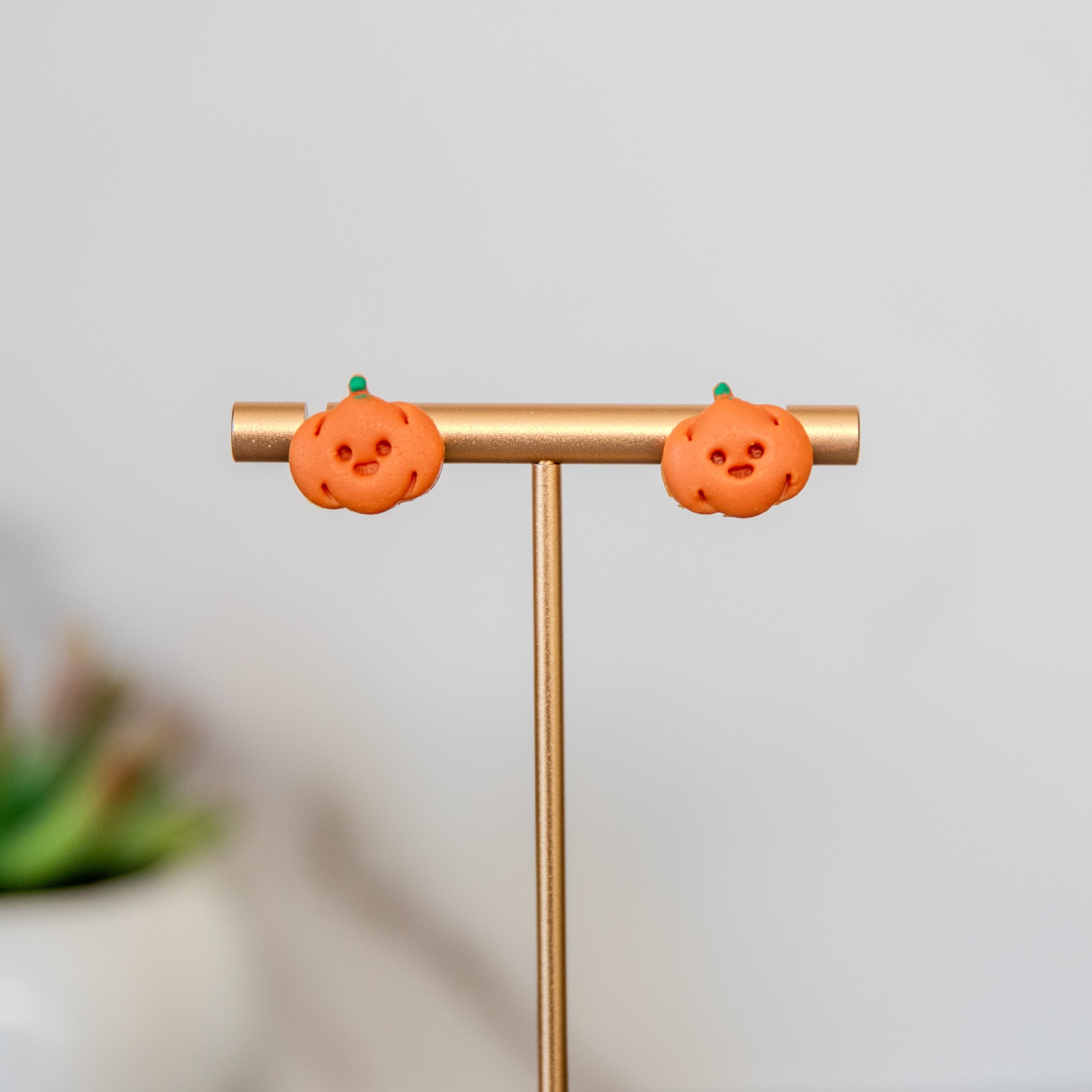 Pumpkin-shaped earrings on a gold stand with a blurred plant in the background