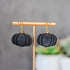 Black pumpkin-shaped earrings on a gold earring stand with a blurred background