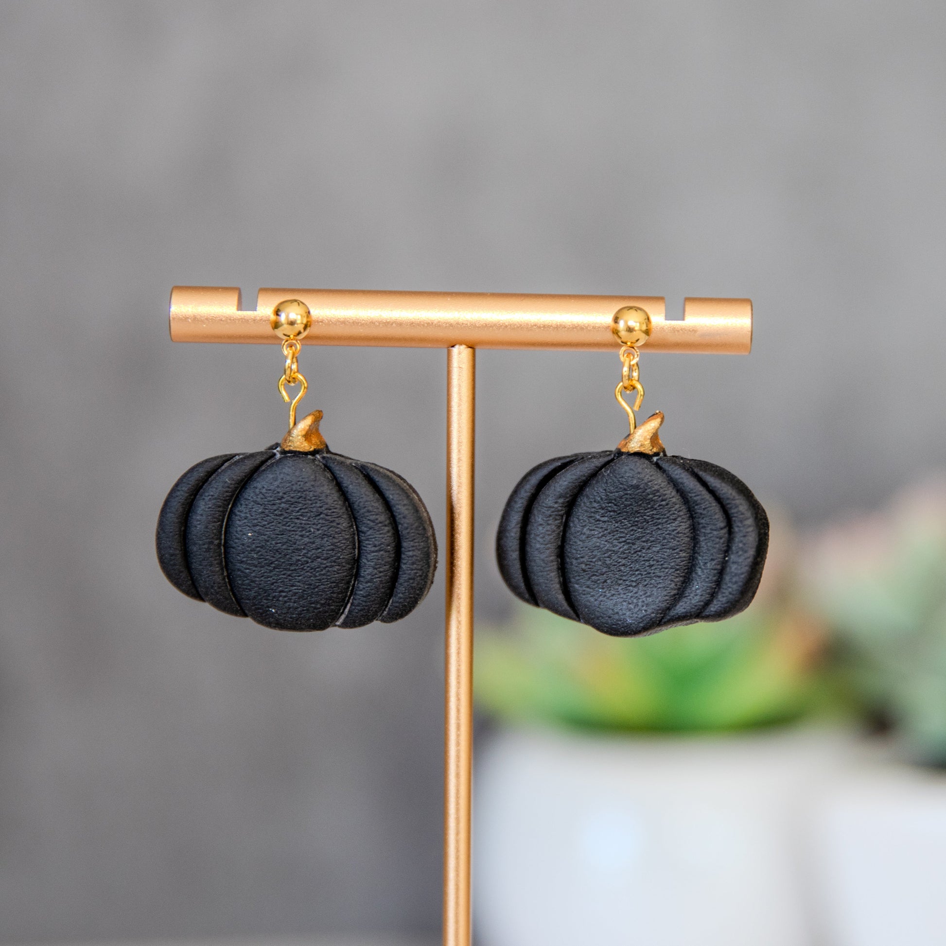 Black pumpkin-shaped earrings on a gold earring stand with a blurred background