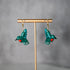 Pair of green bird-shaped earrings on a gold stand against a gray background