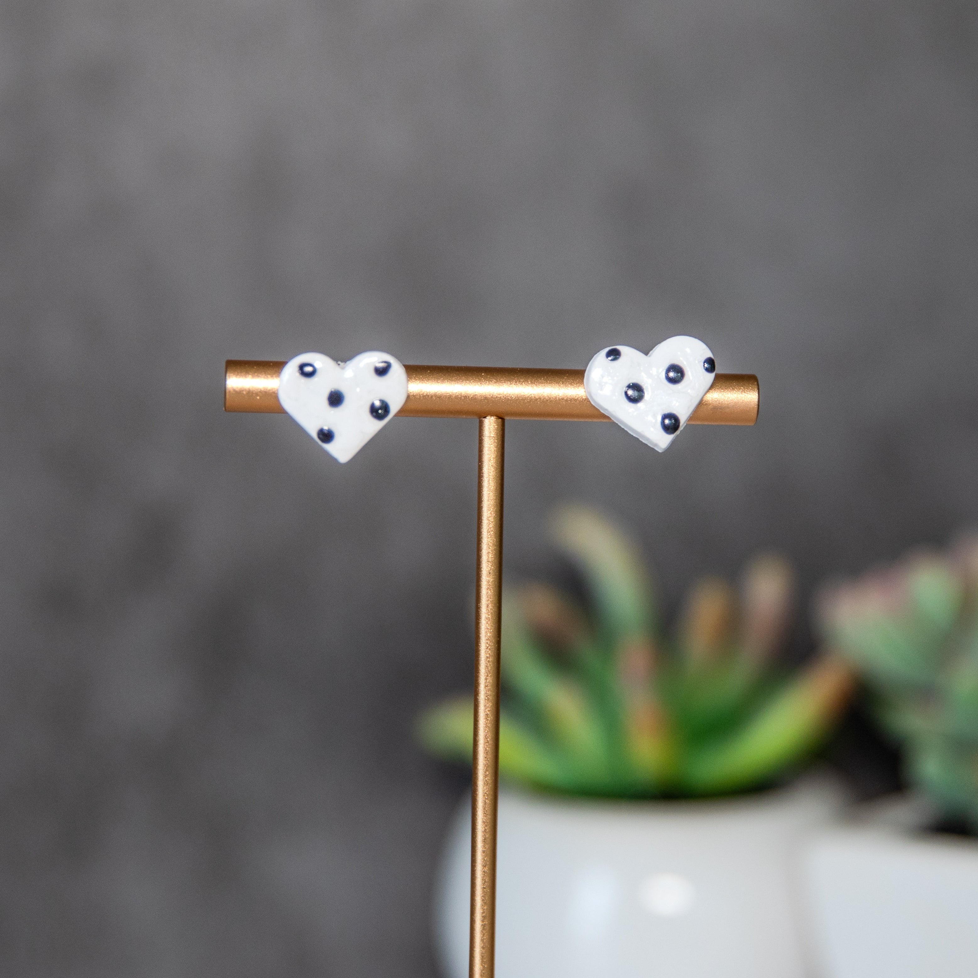 Heart-shaped earrings on a stand with a blurred background and plants.
