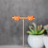 Orange cat-shaped earrings on a gold T-shaped stand with a blurred background