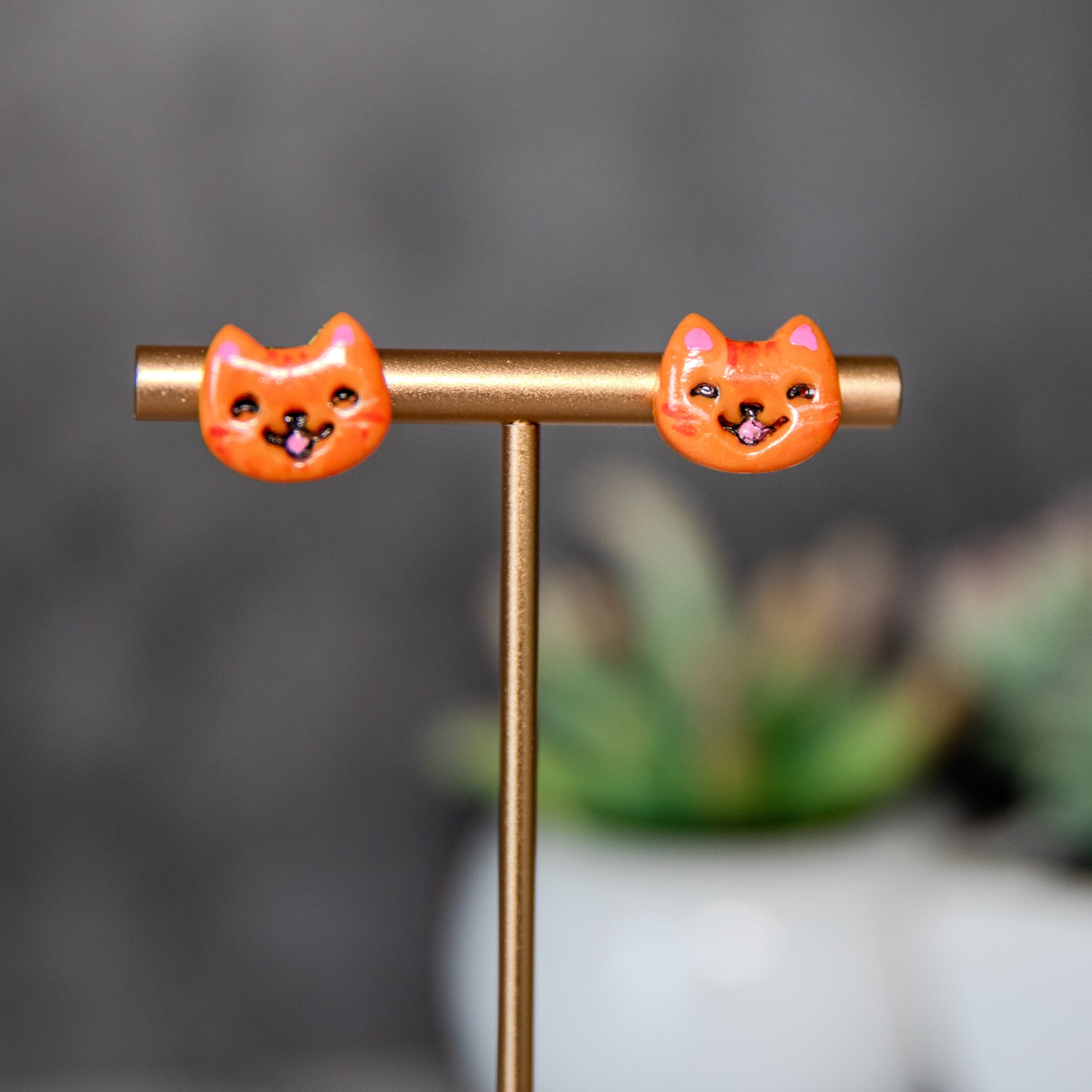 Orange cat-shaped earrings on a gold stand with a blurred background