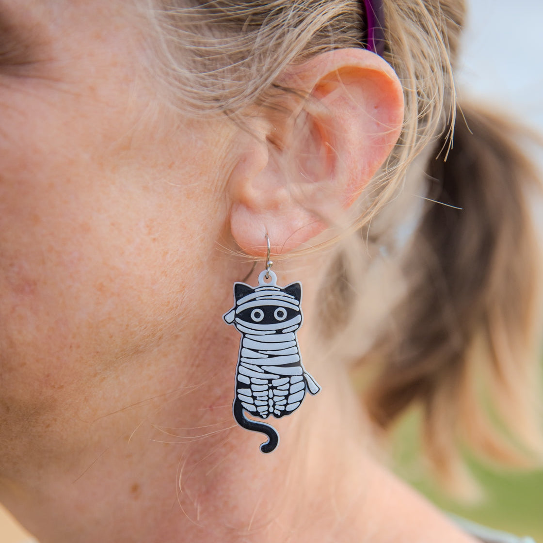 Person wearing a cat-shaped earring with a mummy design.
