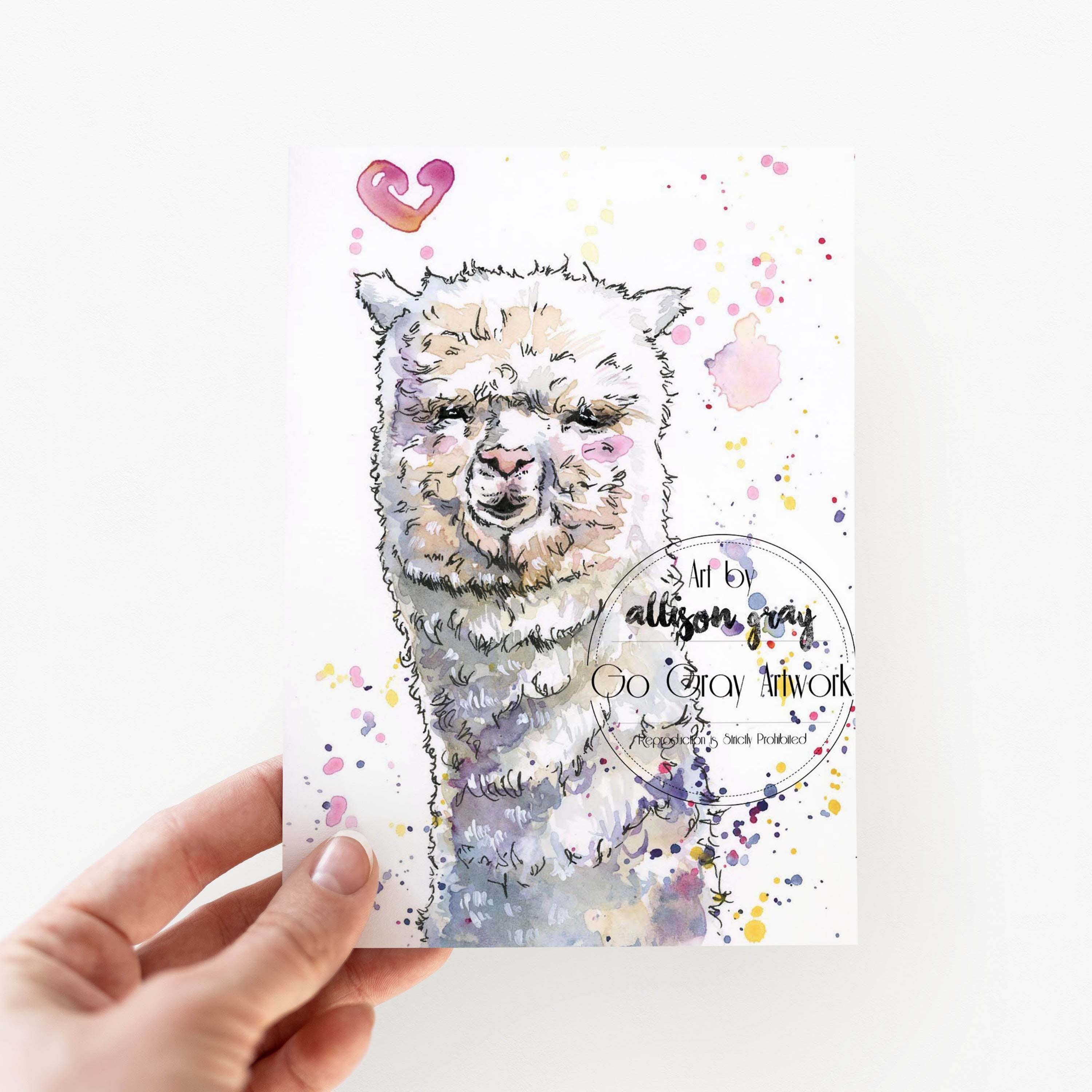 Card with an alpaca illustration and text held by a hand on a white background