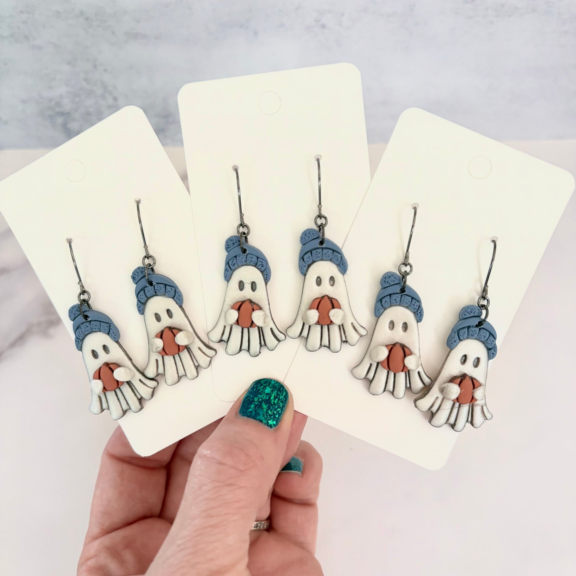 Hanging earrings featuring ghosts holding pumpkins and wearing beanie hats