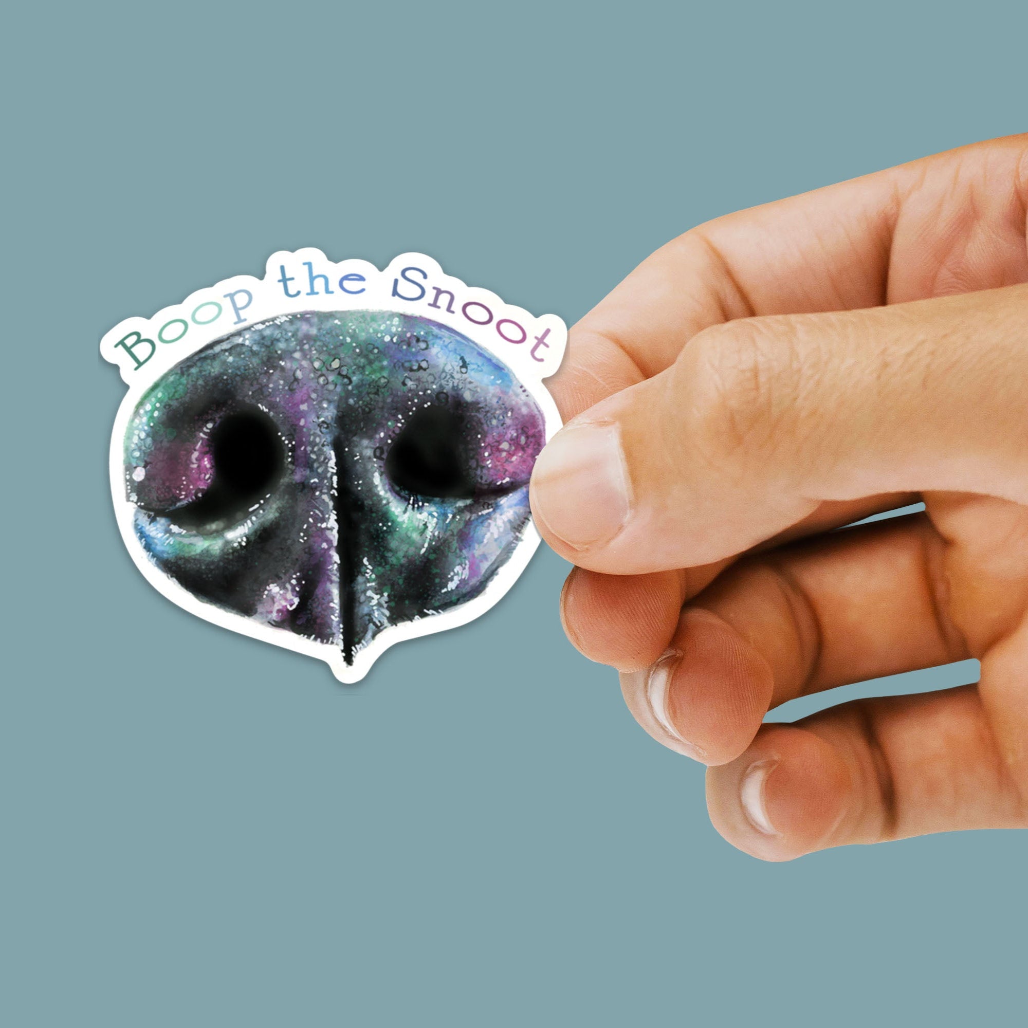 Hand holding a sticker with a colorful dog nose design and 'Boop the Snoot' text on a blue background.