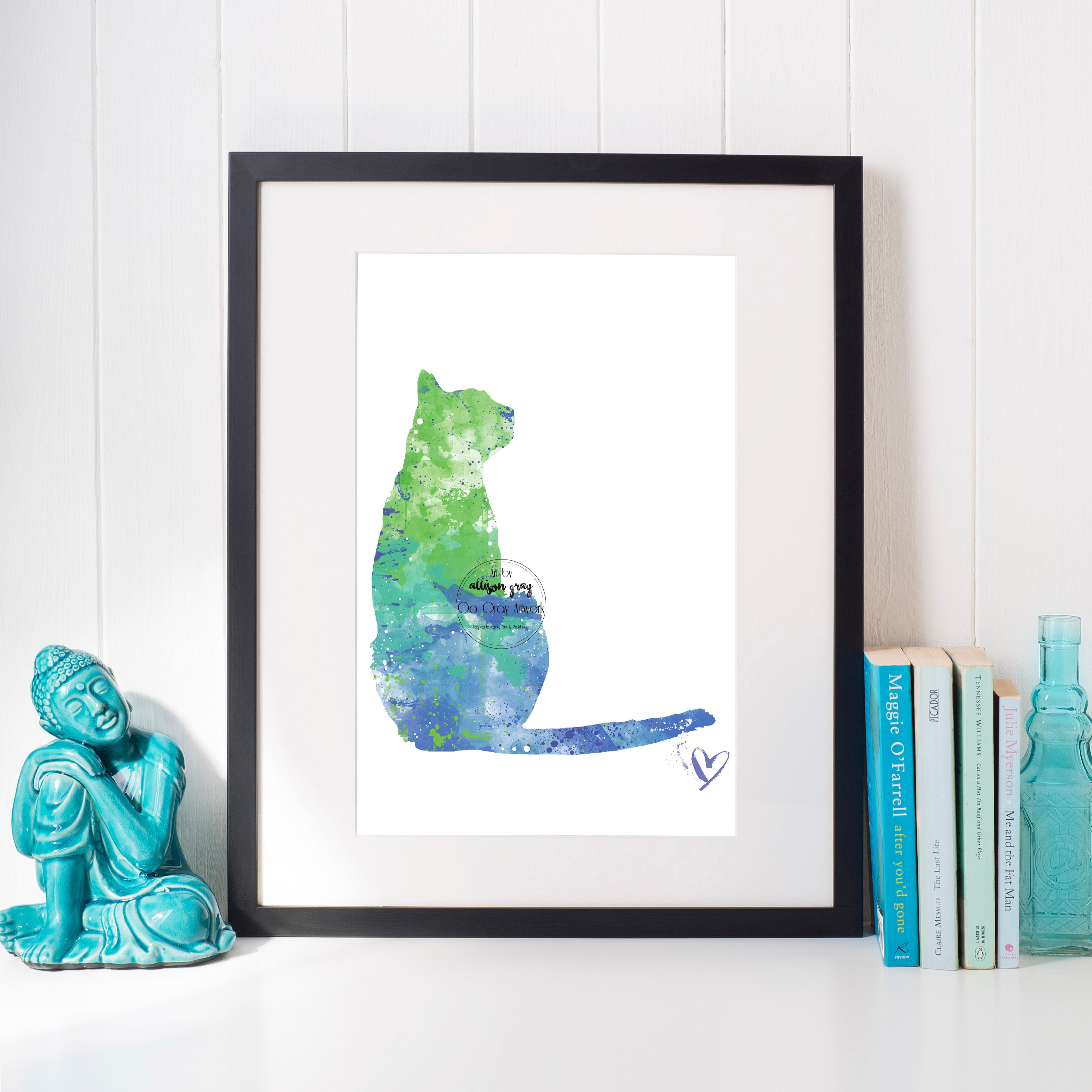 Framed artwork of a colorful cat silhouette on a white wall with decorative items.