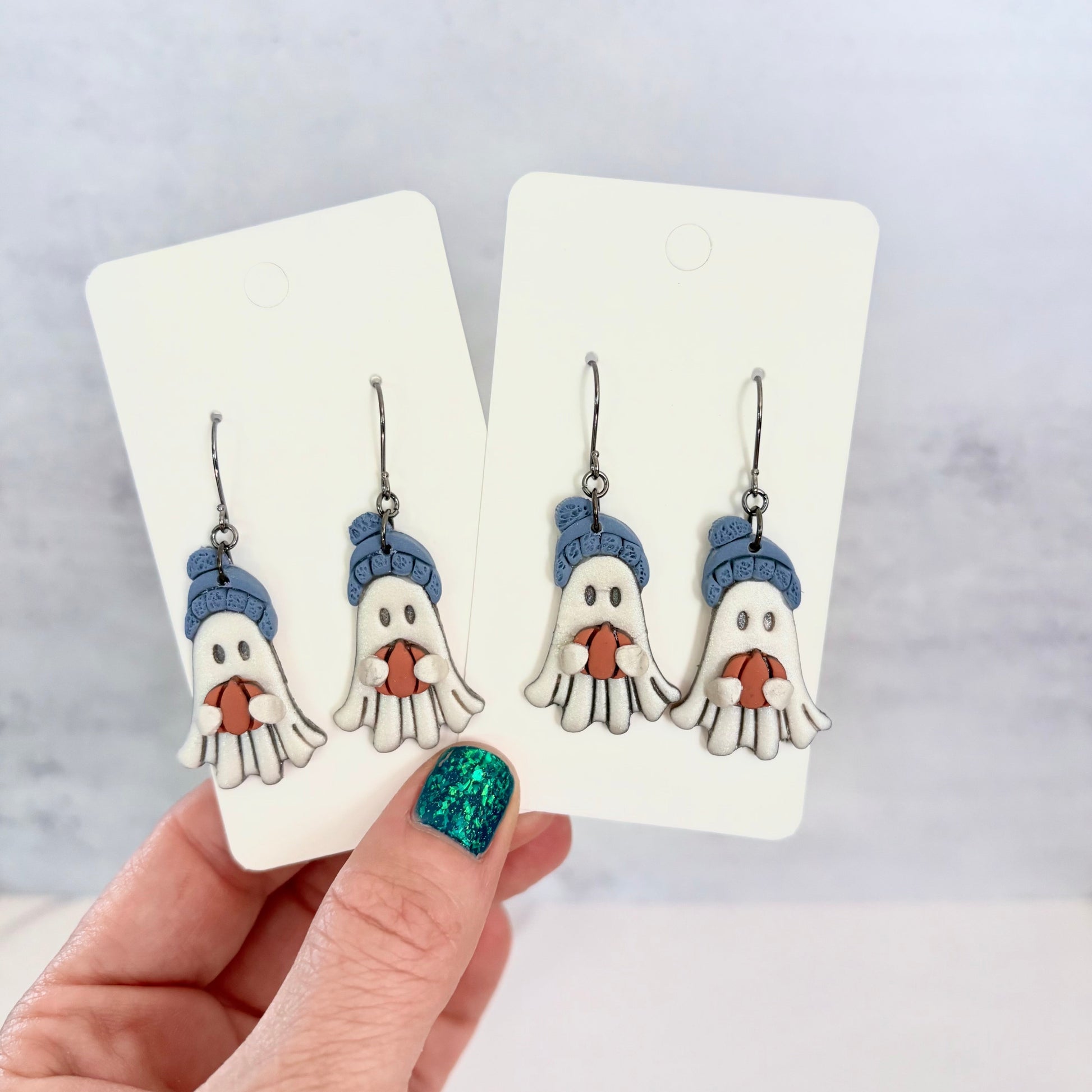 Hanging earrings featuring ghosts holding pumpkins and wearing beanie hats