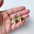 Green mushroom-shaped earrings held in a hand against a white background