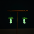 Glowing green mushroom-shaped earrings on a stand against a dark background