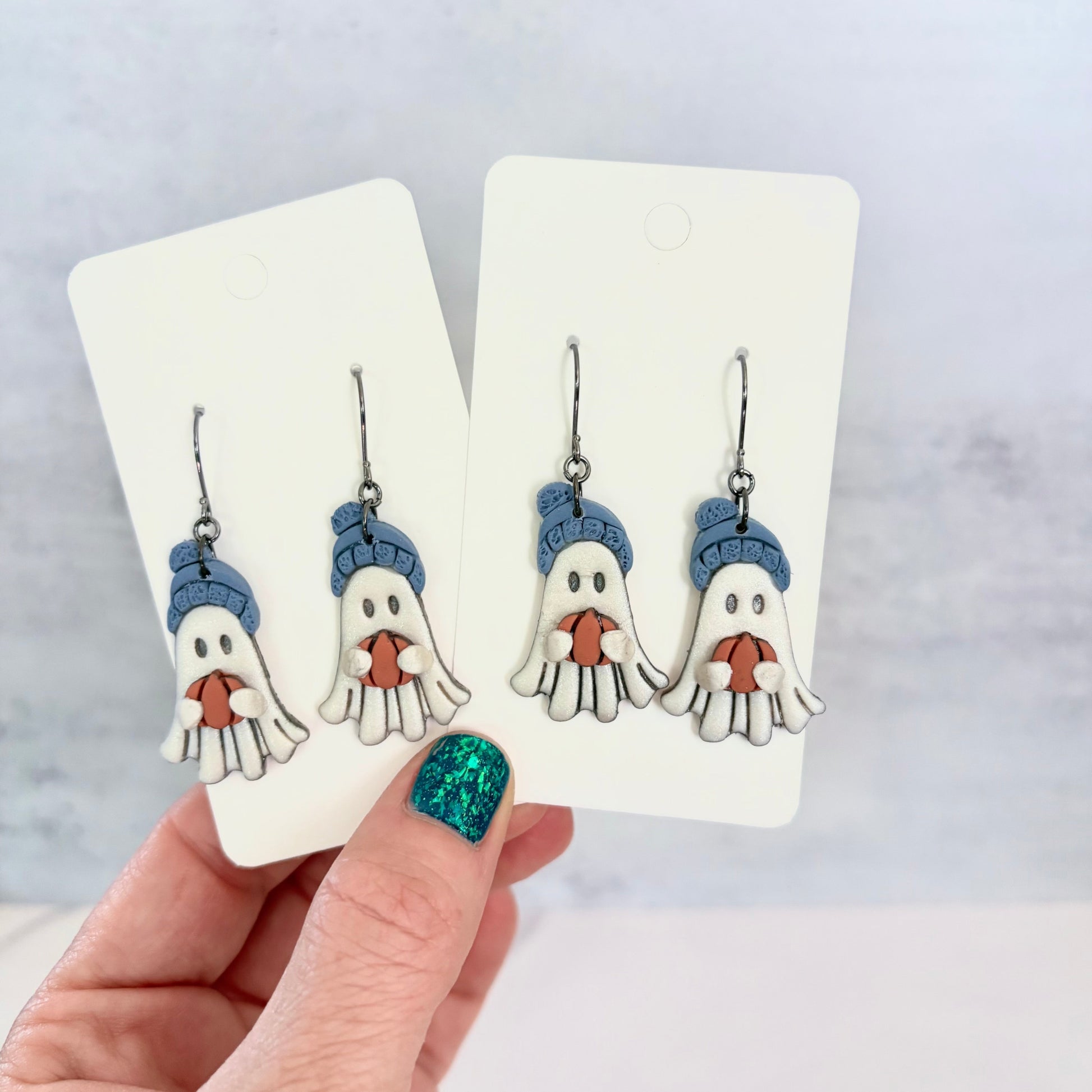 Hanging earrings featuring ghosts holding pumpkins and wearing beanie hats