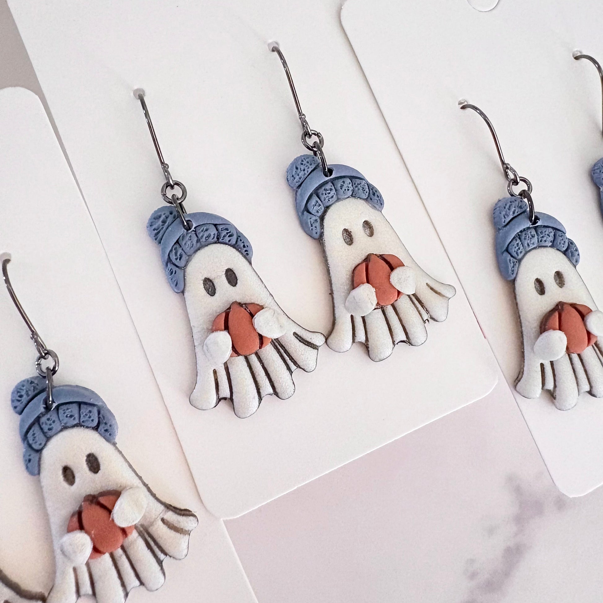 Hanging earrings featuring ghosts holding pumpkins and wearing beanie hats