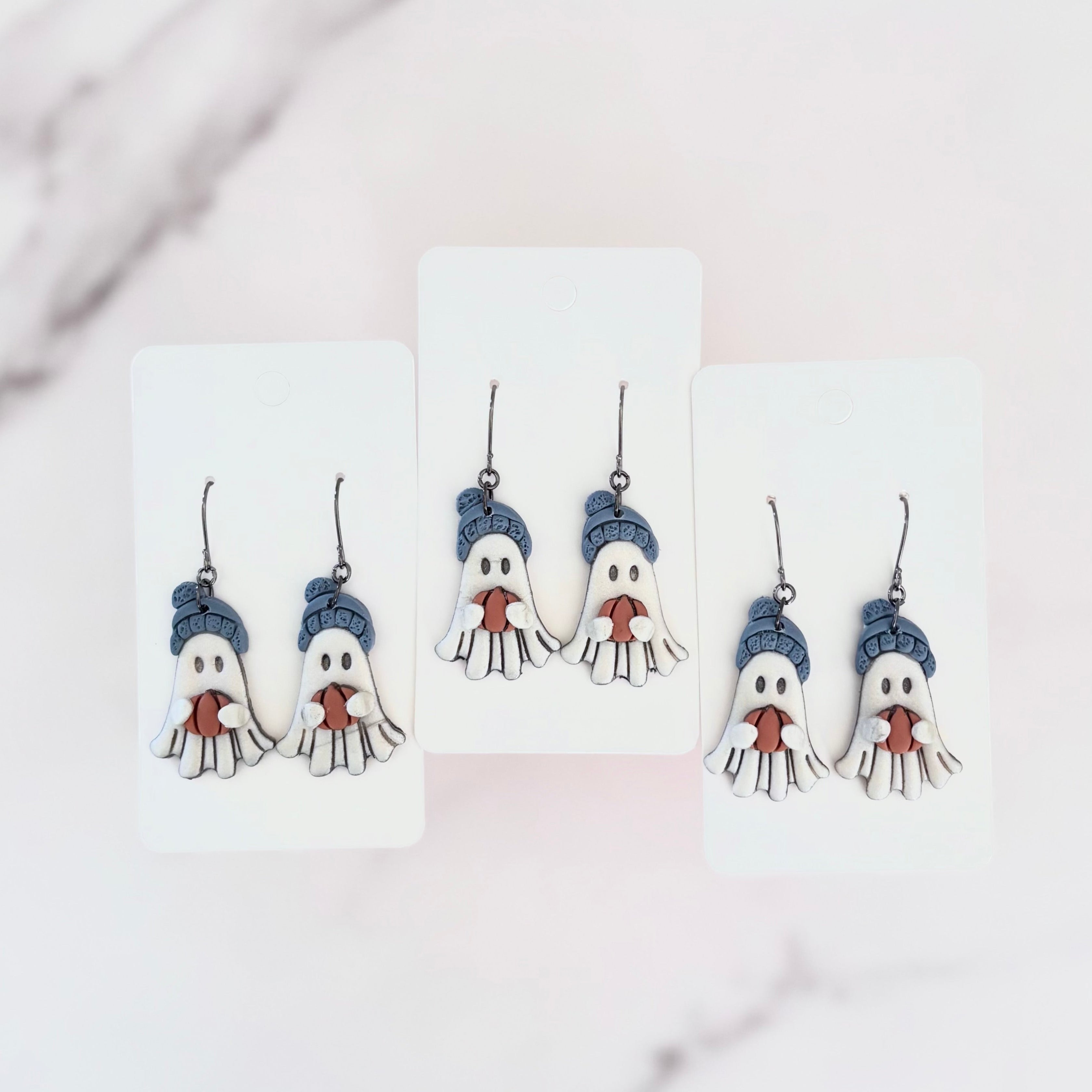 Hanging earrings featuring ghosts holding pumpkins and wearing beanie hats