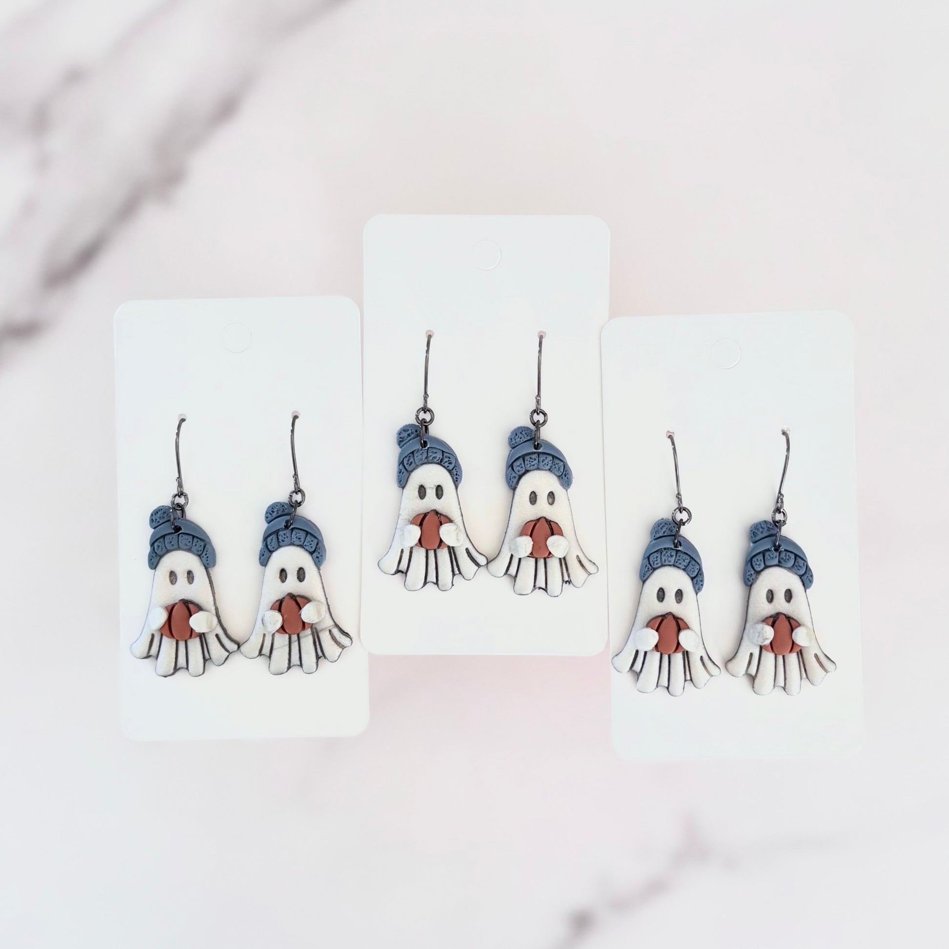 Hanging earrings featuring ghosts holding pumpkins and wearing beanie hats