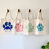 Four tote bags with paw print designs hanging on a wall.
