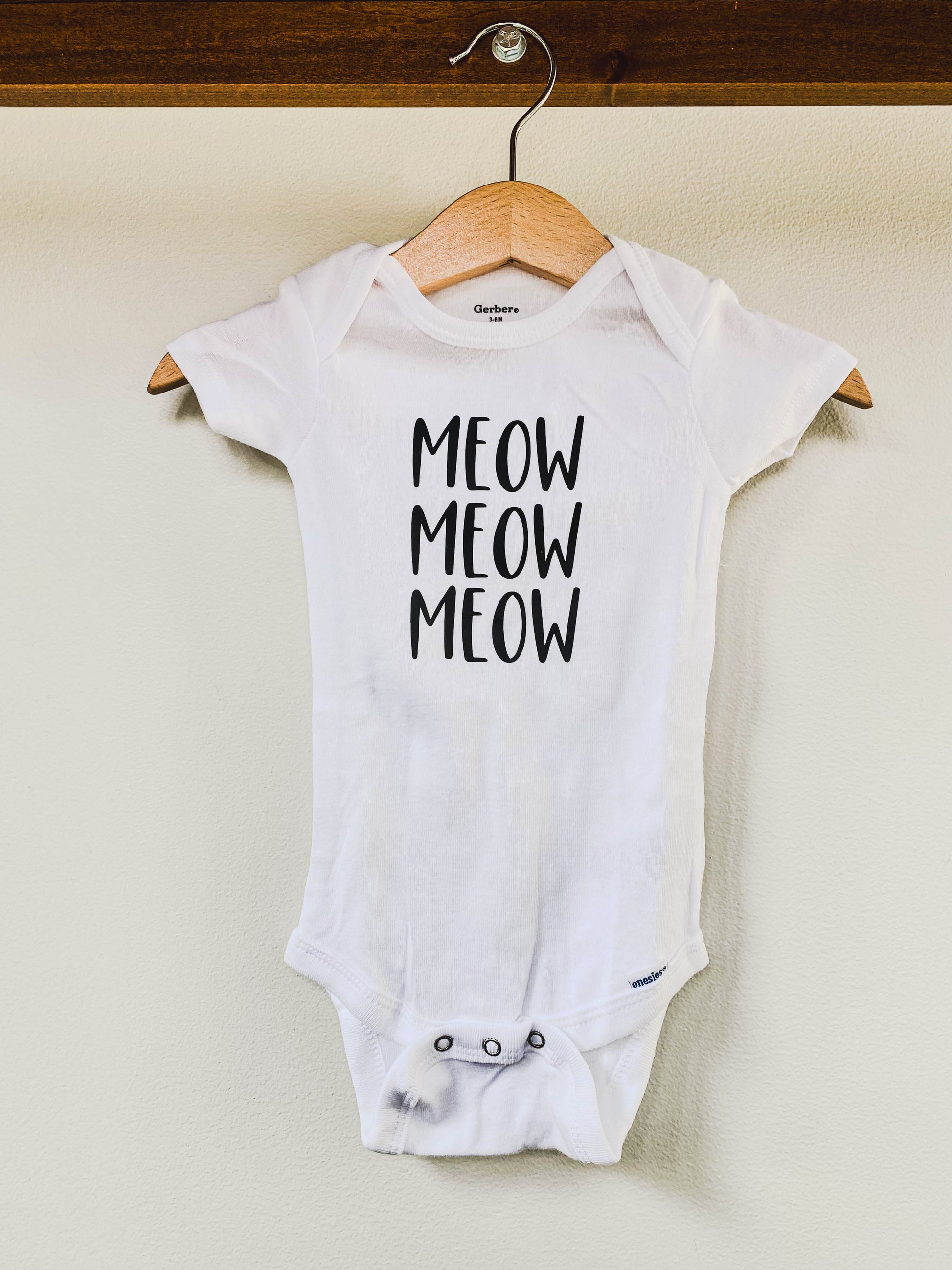 White baby onesie with 'MEOW MEOW MEOW' text 