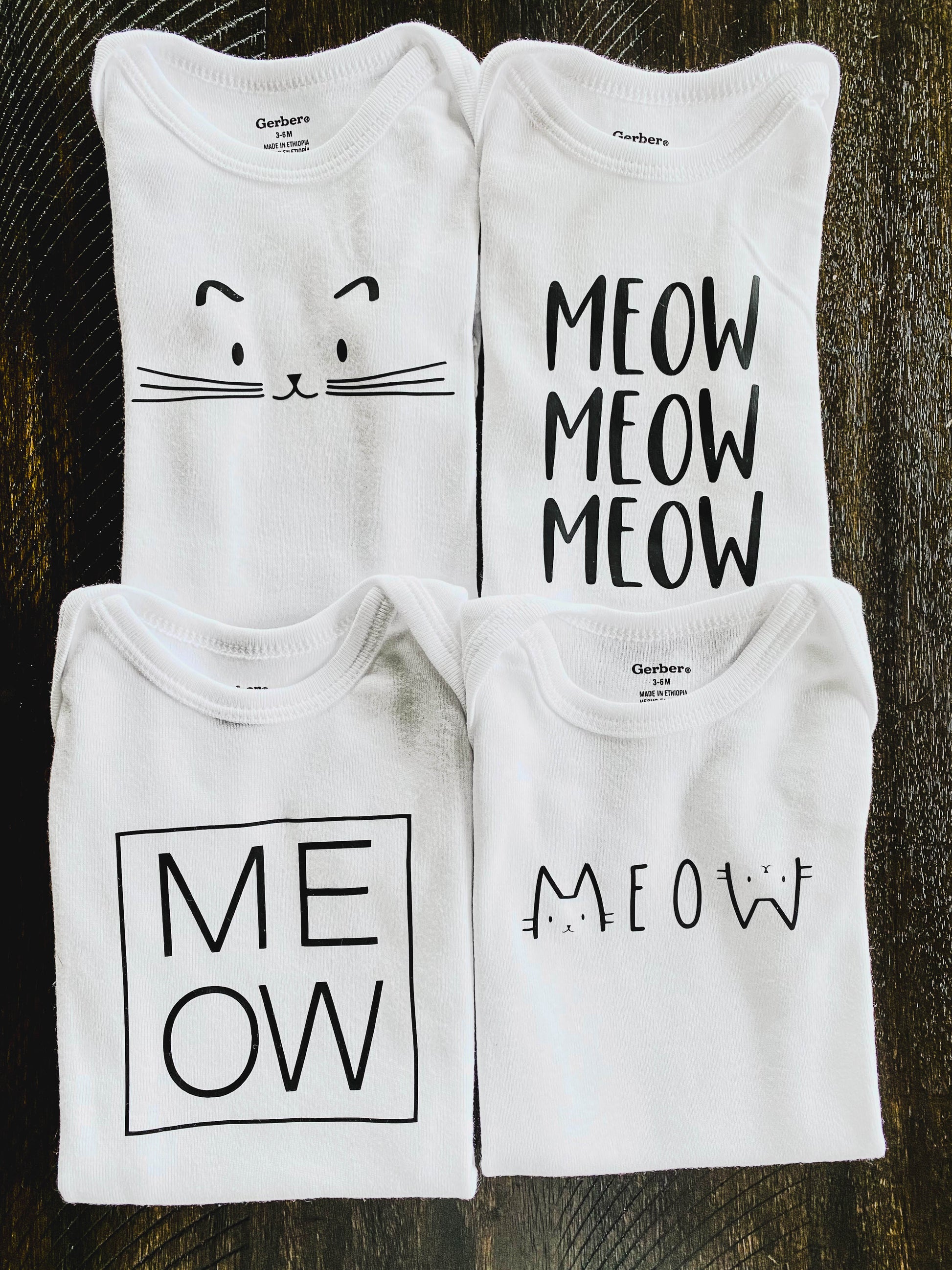 Four white baby onesies with cat-themed designs