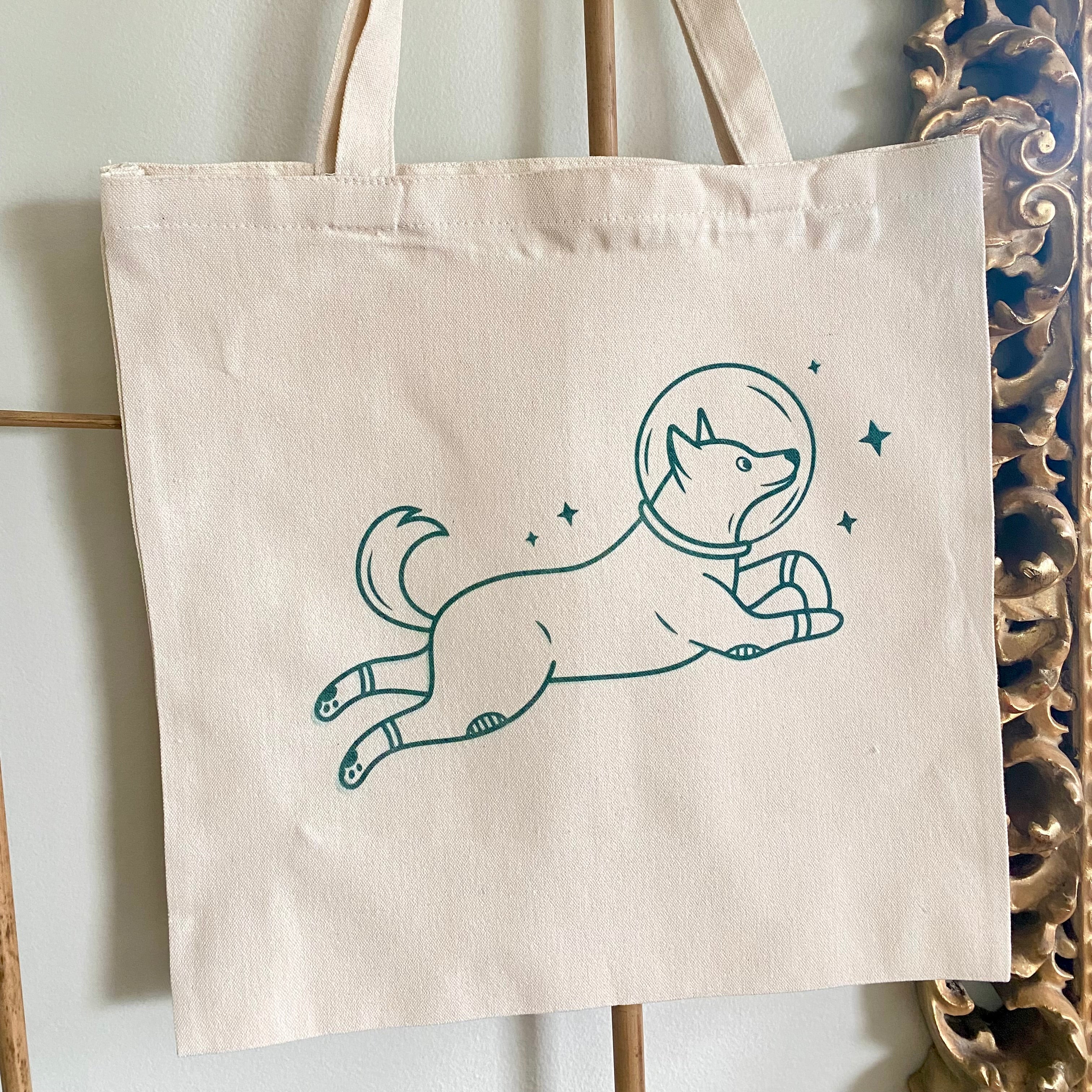 Tote bag with a dog in an astronaut suit design hanging on a rack.
