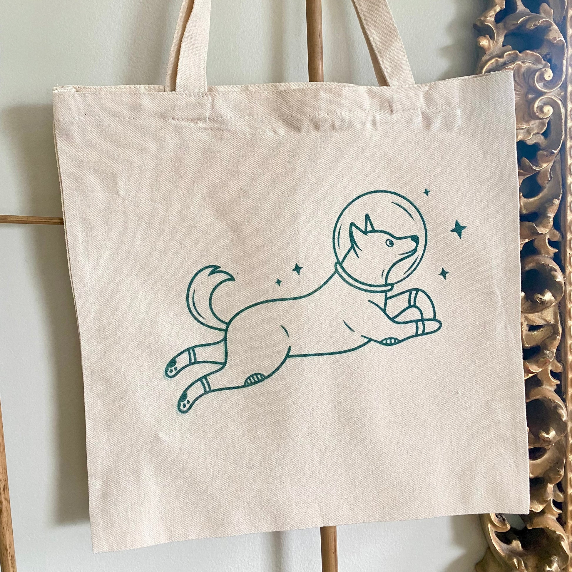 Tote bag with a dog in an astronaut suit design hanging on a rack.