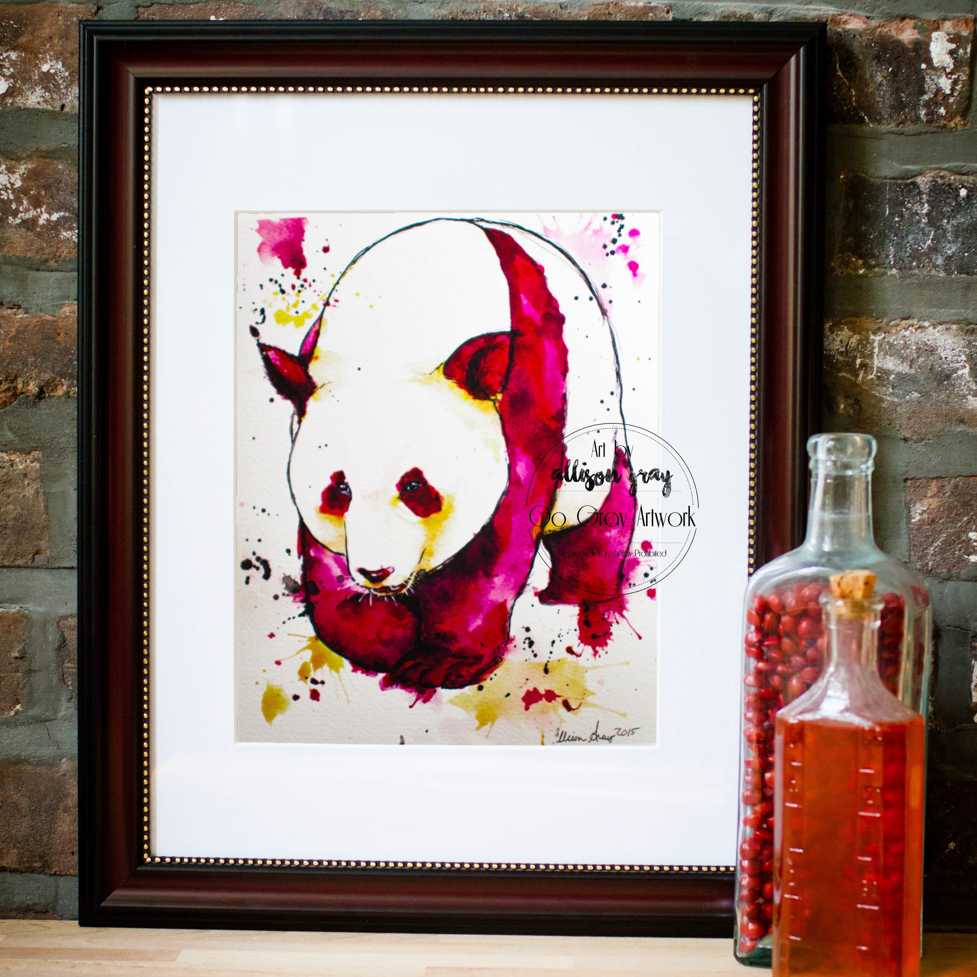 Framed artwork of a colorful panda on a brick wall background with a bottle of liquid.