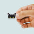 Hand holding a black cat sticker with yellow eyes on a light gray background