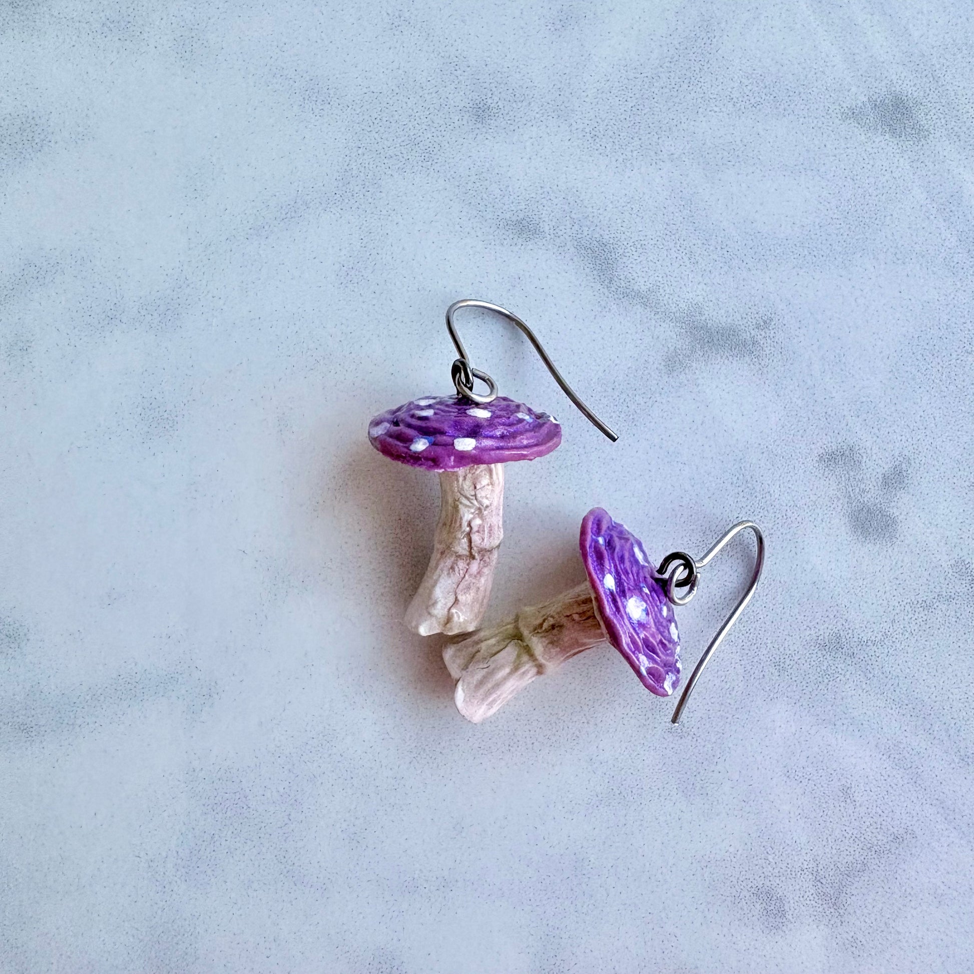 Mushroom-shaped earrings with purple caps on a light gray background