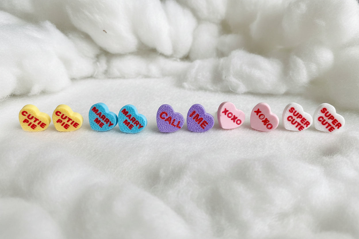 Heart-shaped candy earrings with various text on a gray background
