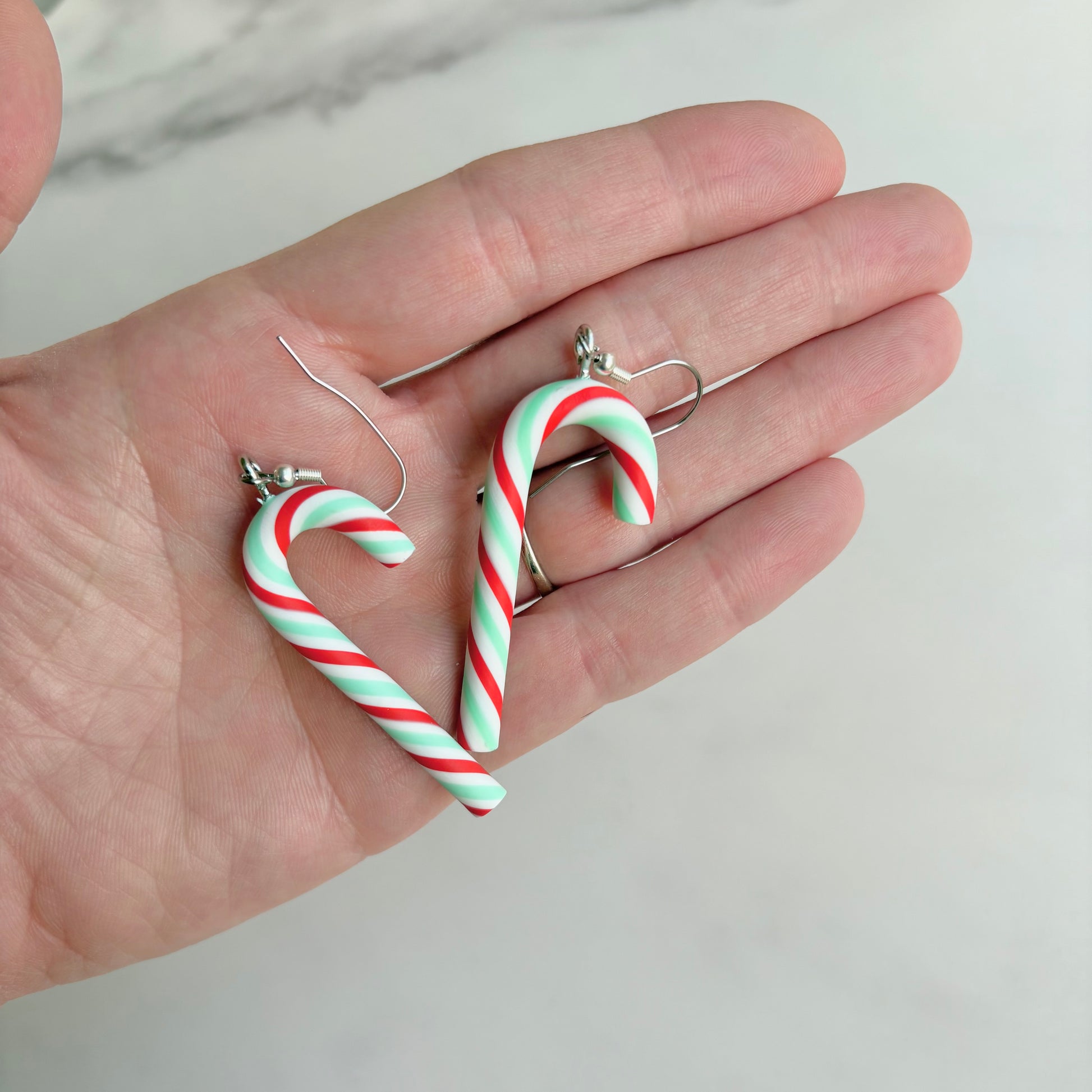 Candy cane-shaped earrings held in a hand against a neutral background