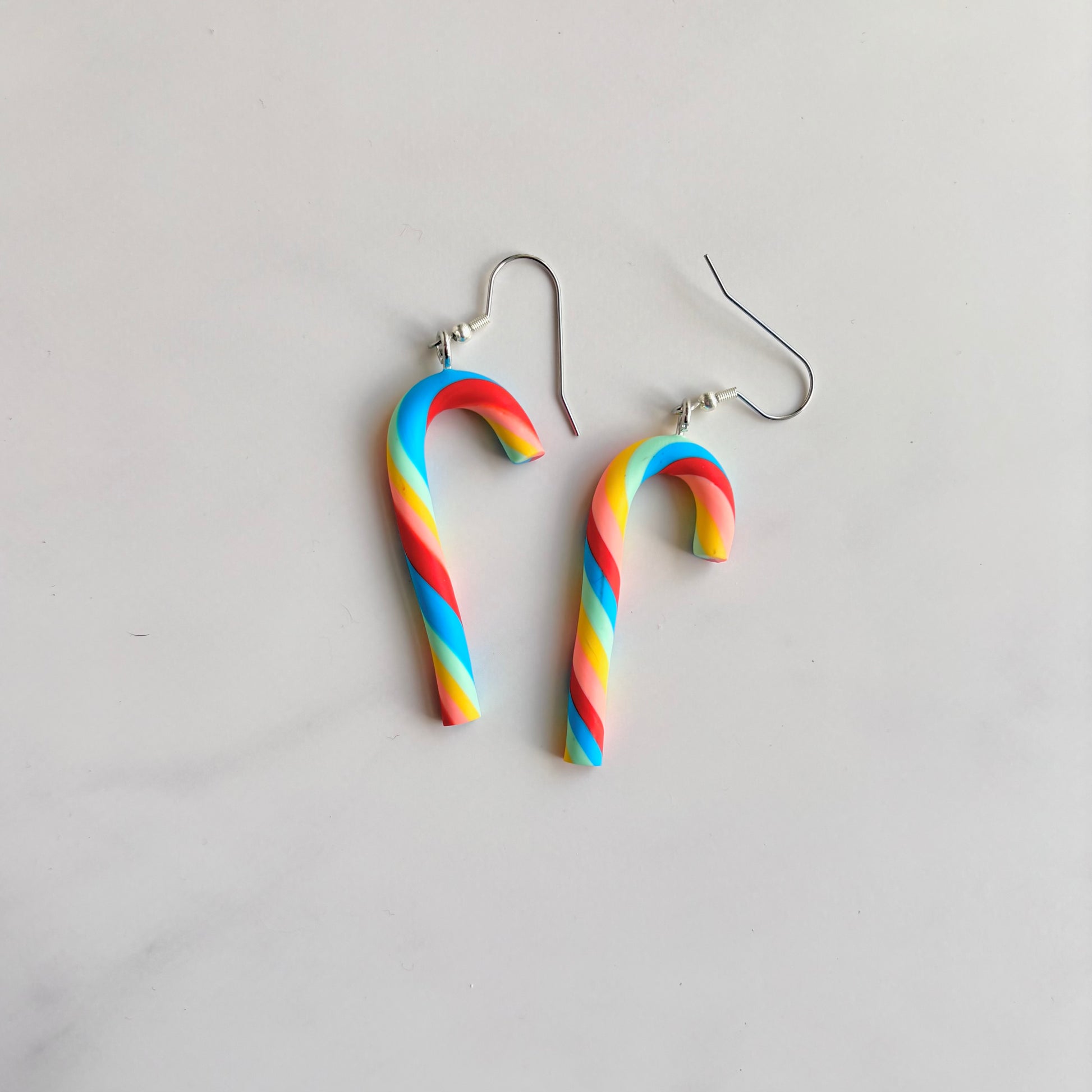 Rainbow candy cane-shaped earrings on a light gray background